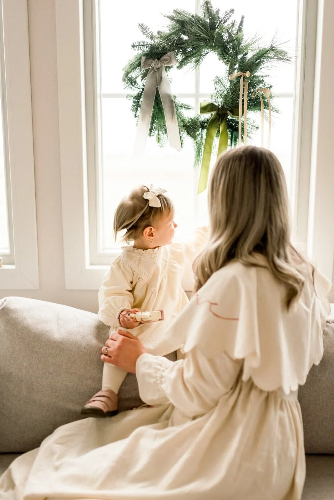 A mother holding her little girl beside a window decorated for Christmas.