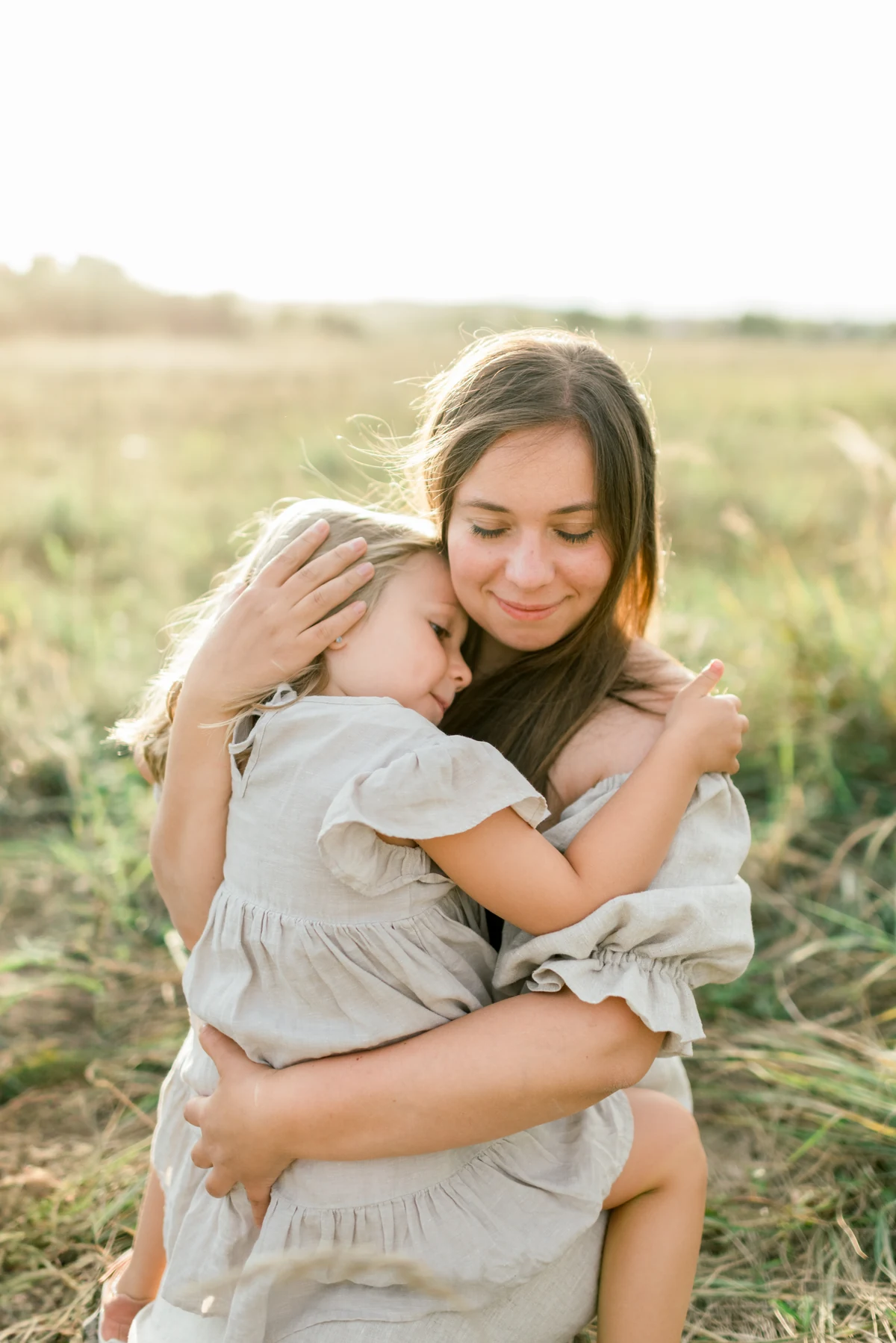 A mother closes her eyes as she hugs her little girl in the grass.