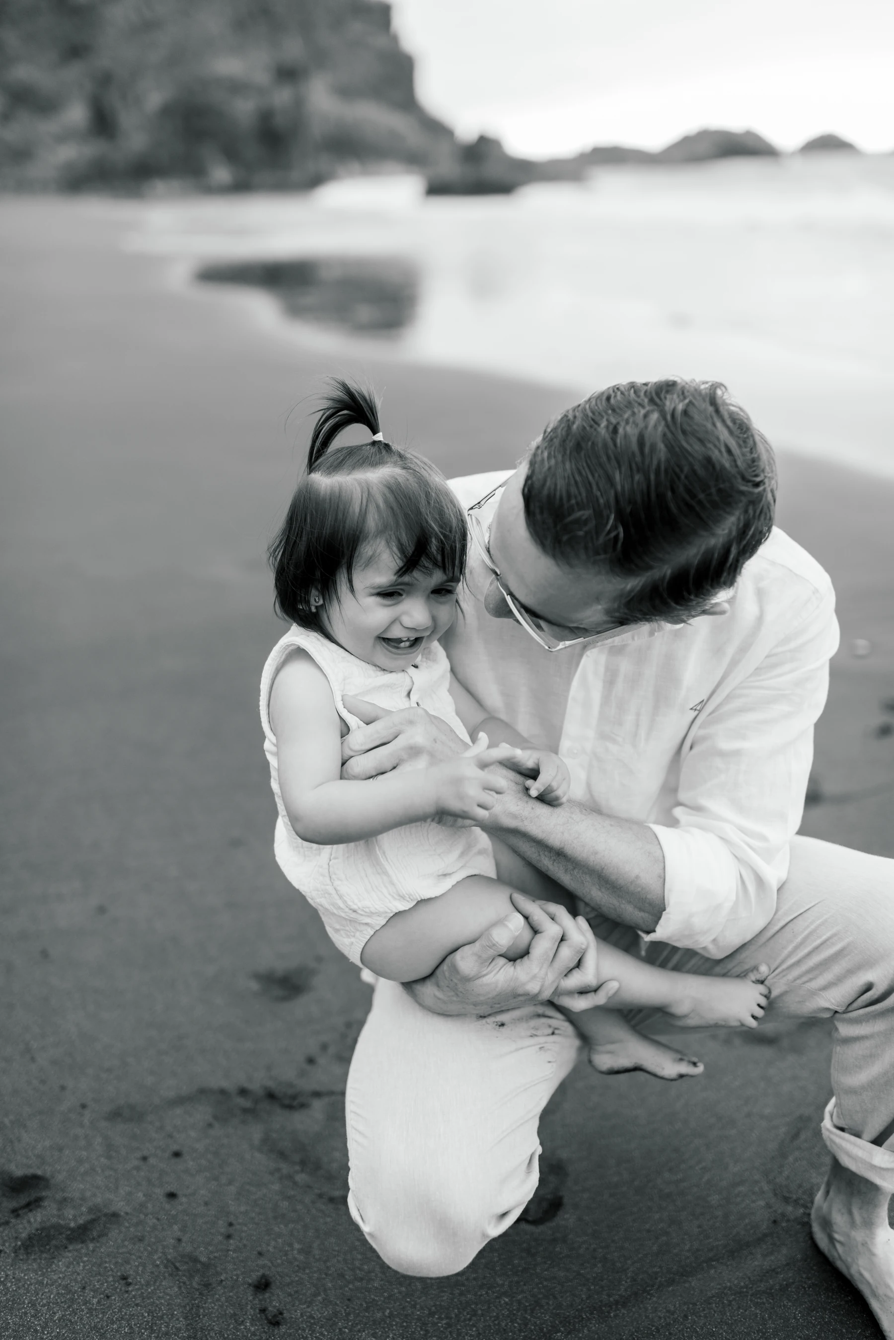 A father looking at his laughing daughter in his arms, in black and white.