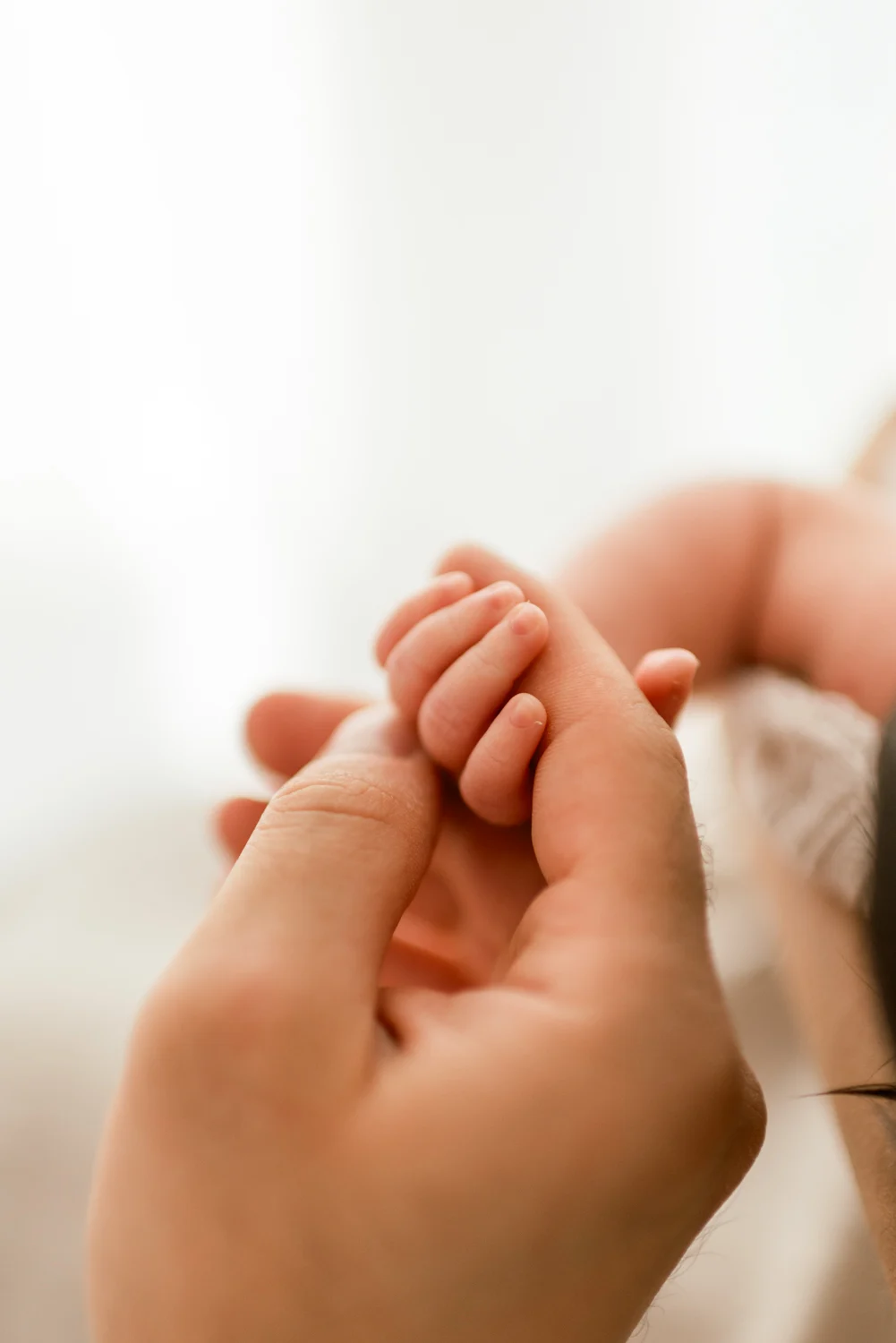 A baby’s hand curled around a parent’s finger.
