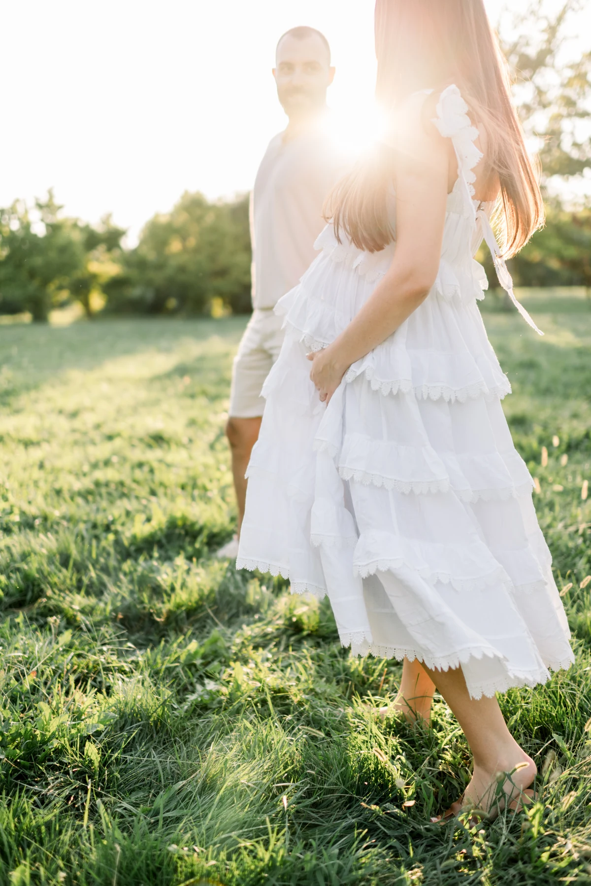 An expectant mother and her partner embracing in a garden in warm sunlight.