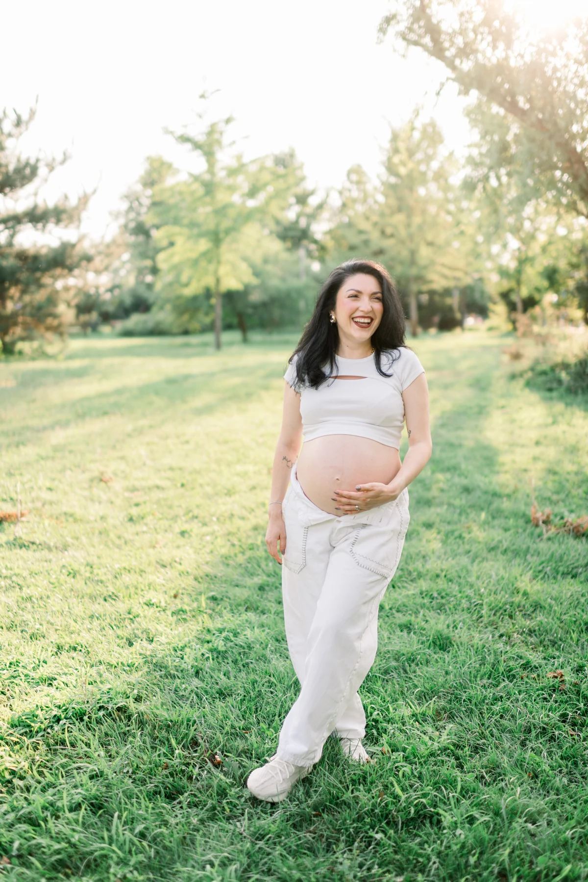 An expectant mother smiling barefoot in a garden, her hands on her bump.