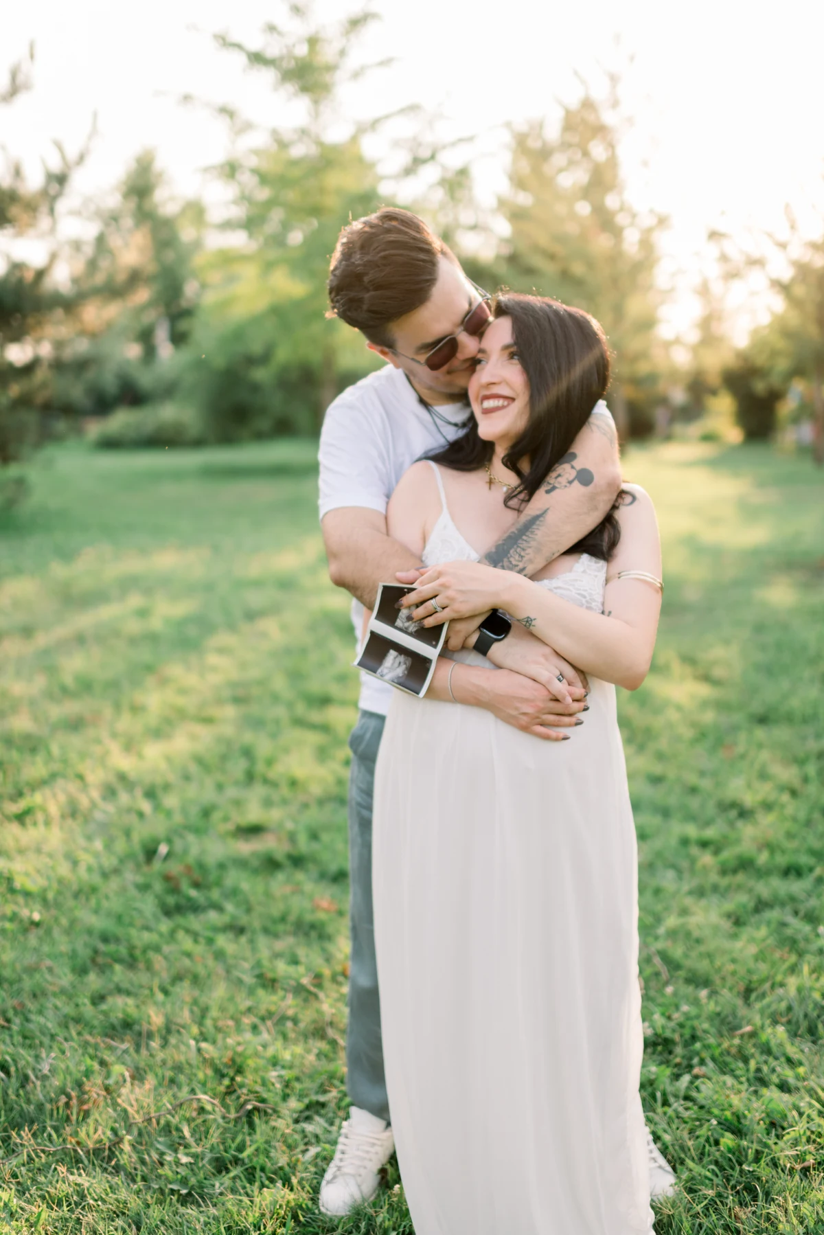 Parents-to-be embracing in a garden, holding their ultrasound photographs.