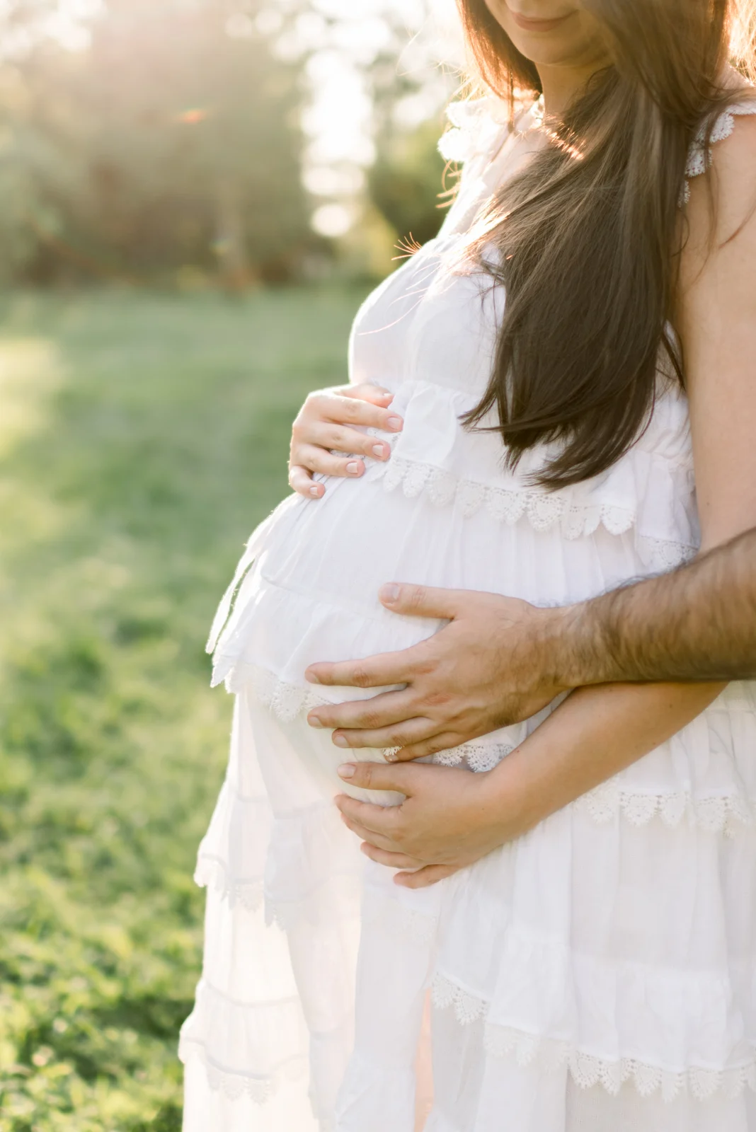 The parents-to-be rest their hands together on the mother’s bump.