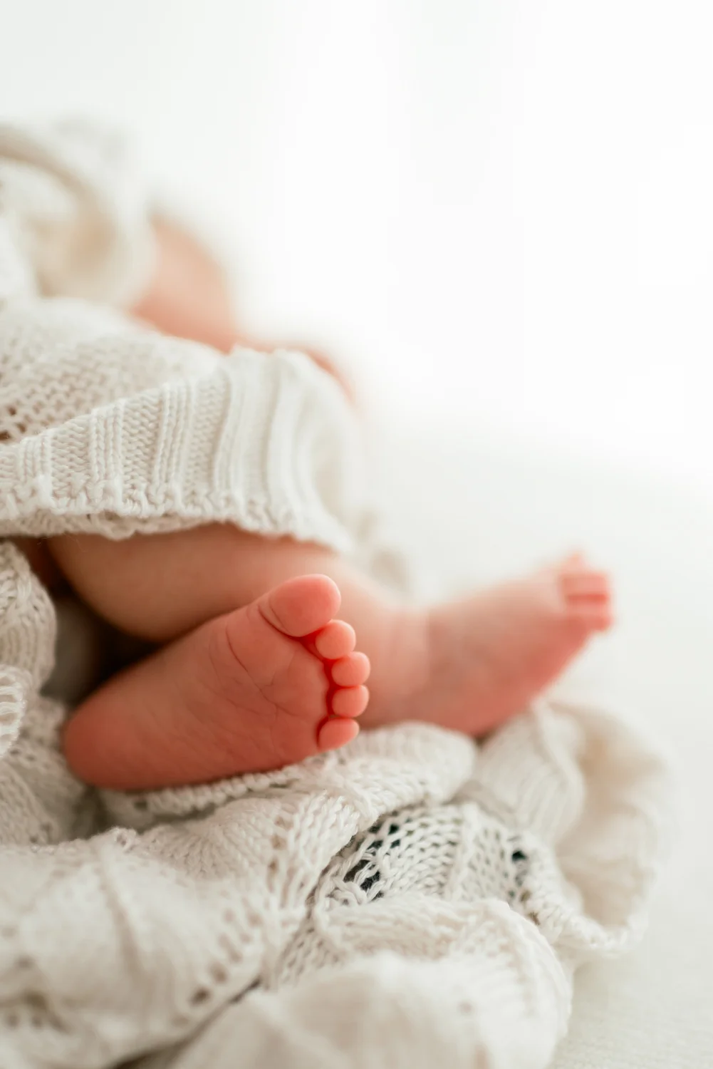 A newborn’s tiny feet peeking out of a white knitted blanket.