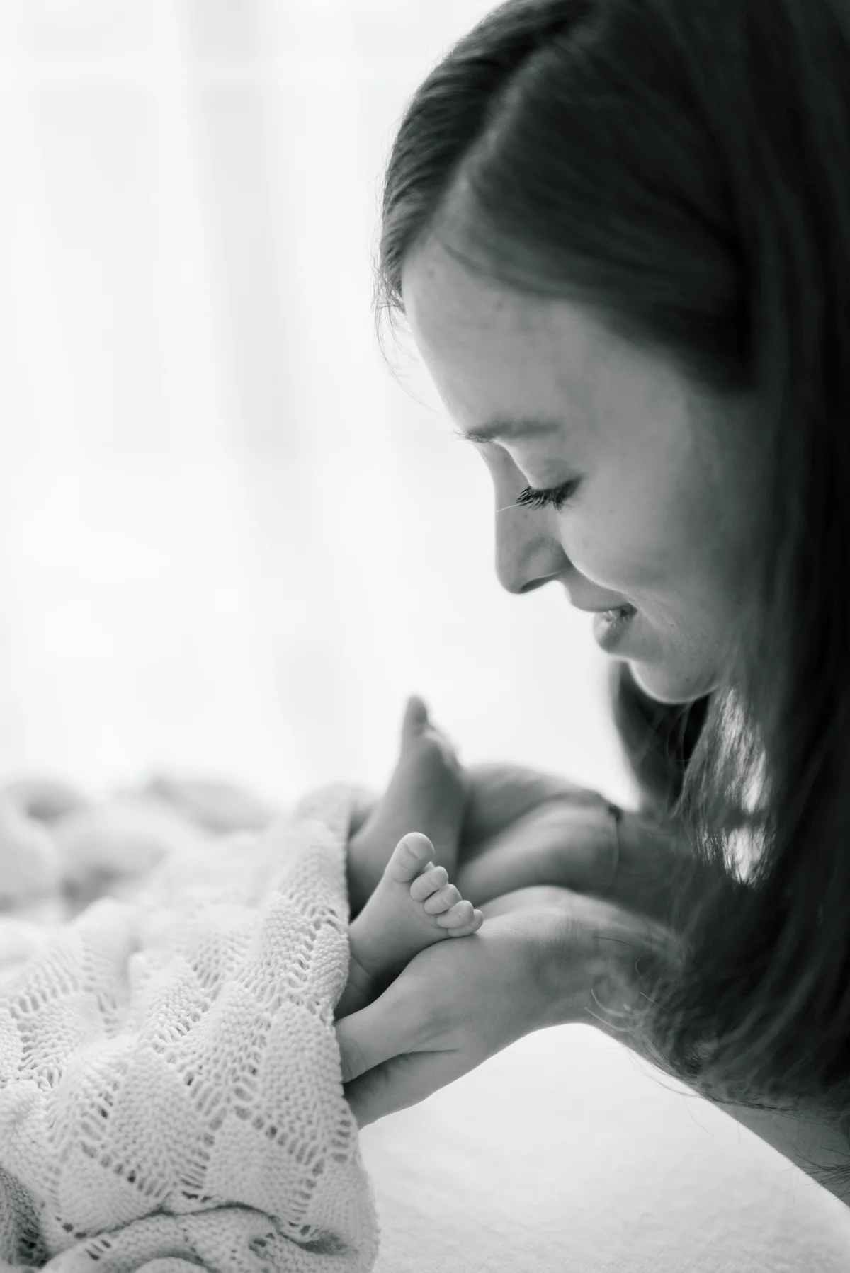 A mother kissing her sleeping newborn’s hand, in black and white.