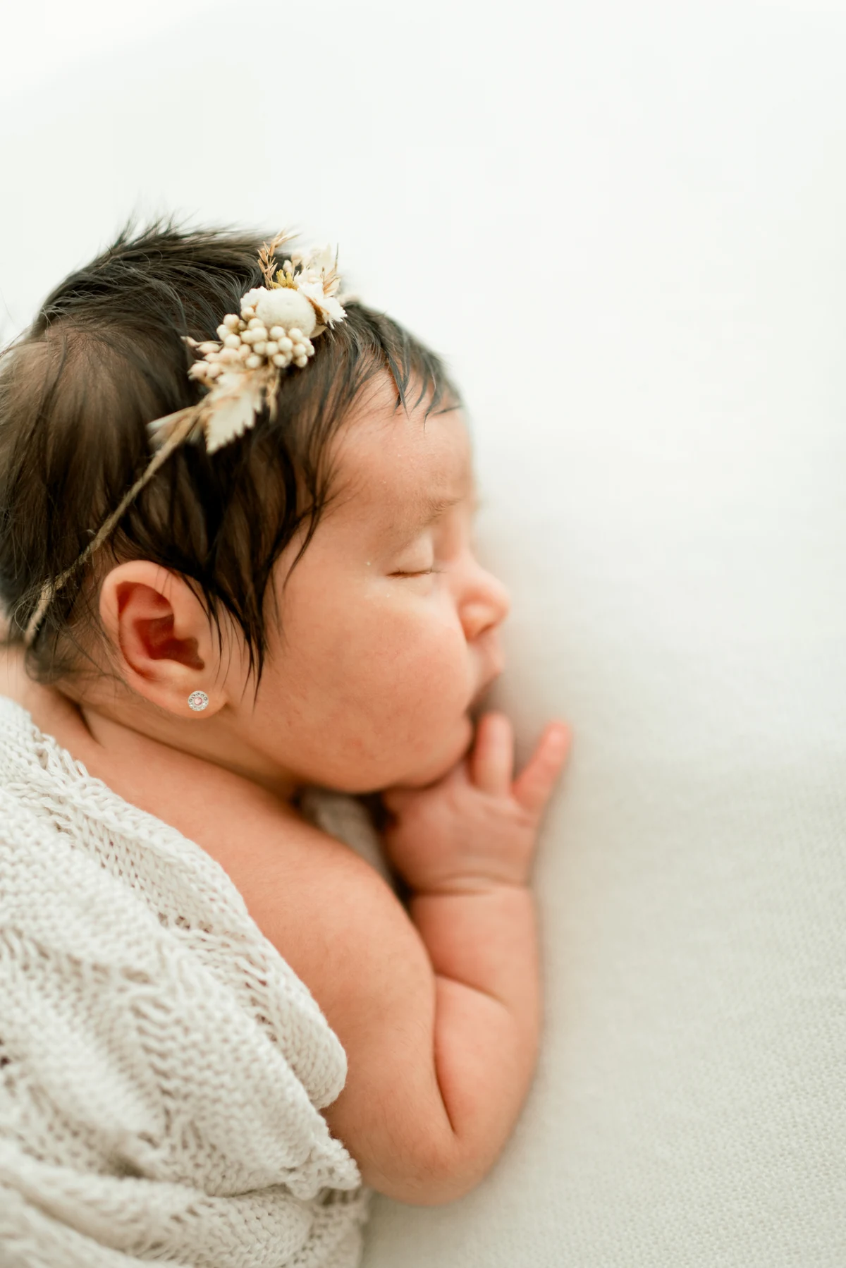 A sleeping baby with their hands beside their cheek, wrapped in a light blanket.