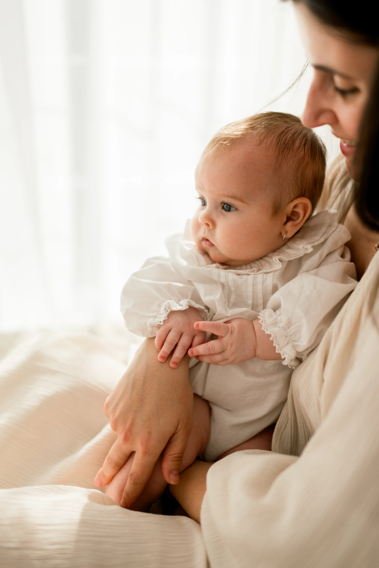 A mother holding her baby beside a bright window.