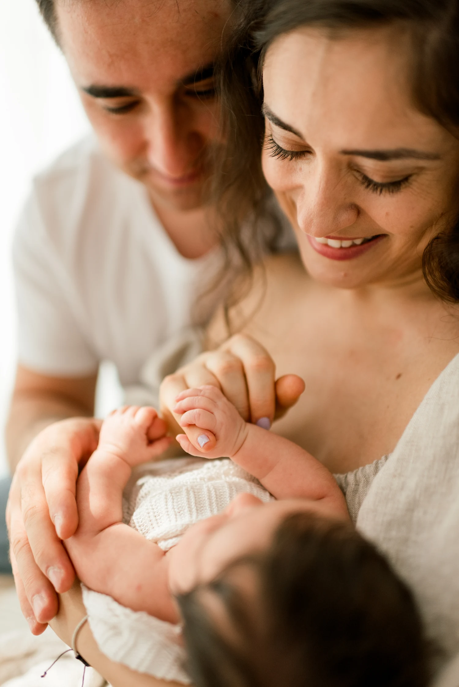 Two parents gazing at their baby asleep in their arms.